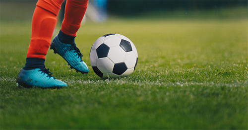 Athlete in blue cleats kicks soccer ball